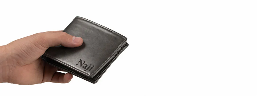 Hand holding a grey wallet engraved with the name Naji